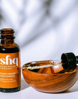 Ishq organic beard oil bottle with wooden bowl and dropper on a light background